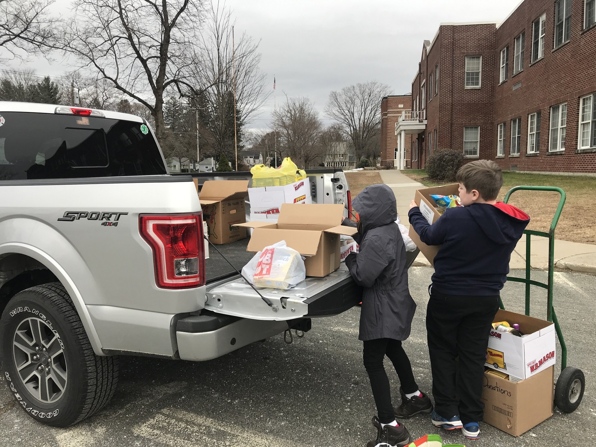 Two 4th grade students help load food drive donations onto a truck.